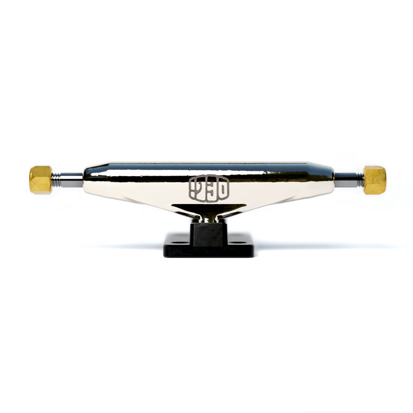 A close-up of a Deli Trucks Black skateboard truck by tiny skateshop features a polished silver body with gold nuts at each end. The brand logo is displayed centrally on the truck, while the black baseplate contrasts against a plain white background.
