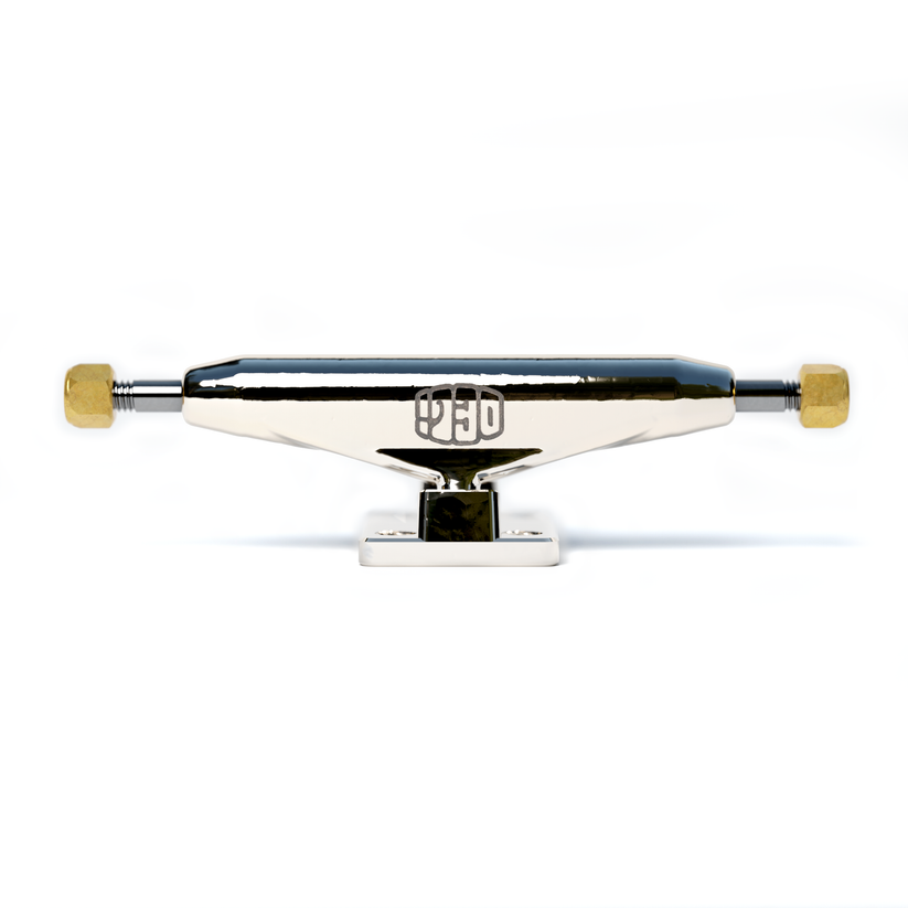 The Deli Trucks Silver from tiny skateshop features a sleek, polished silver design with gold-toned axle ends and a centered logo, all set against a white background.